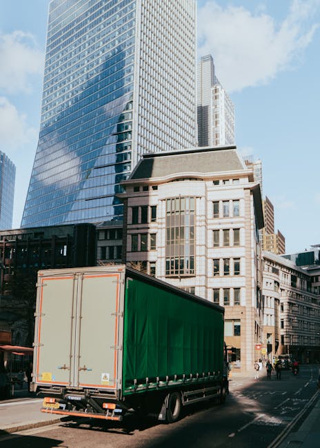 The back of a white van parked on a city street, with its rear doors open revealing various packed boxes made of cardboard and plastic, some with labels, and large white and black garbage bags filled